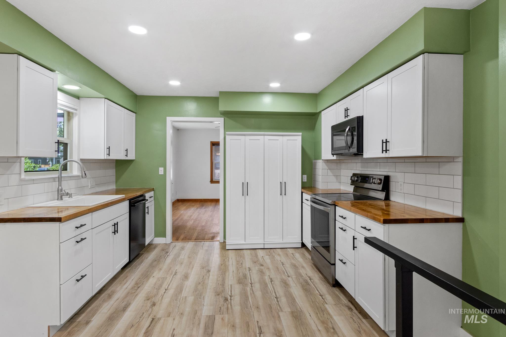 Modern kitchen featuring white shaker cabinetry with matte black hardware, wood-finish countertops, and a white subway tile backsplash