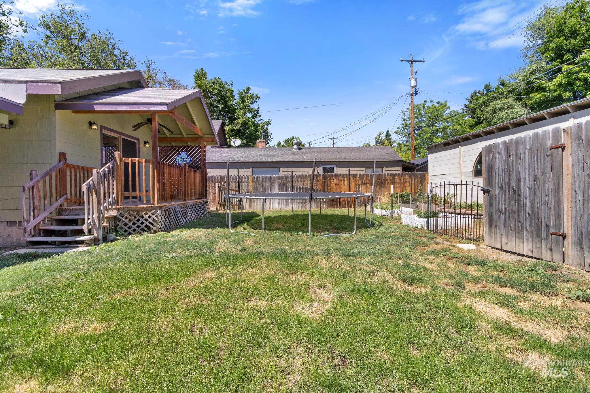 Expansive backyard featuring a covered deck with wood railing, a level lawn, a wood-sided outbuilding, and a decorative metal gate