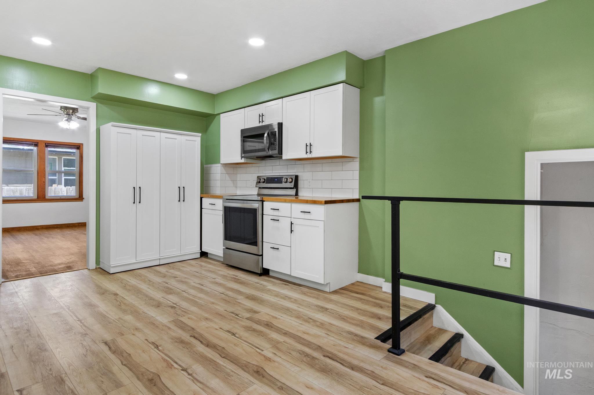 Kitchen space featuring wood-finish flooring, white cabinetry with contemporary black hardware, stainless steel appliances, and a wood-finish countertop