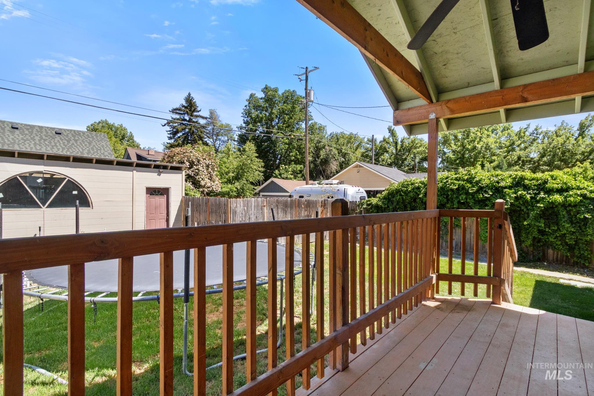 Covered deck with wood-finish flooring and a ceiling fan, overlooking a fenced backyard with green lawn
