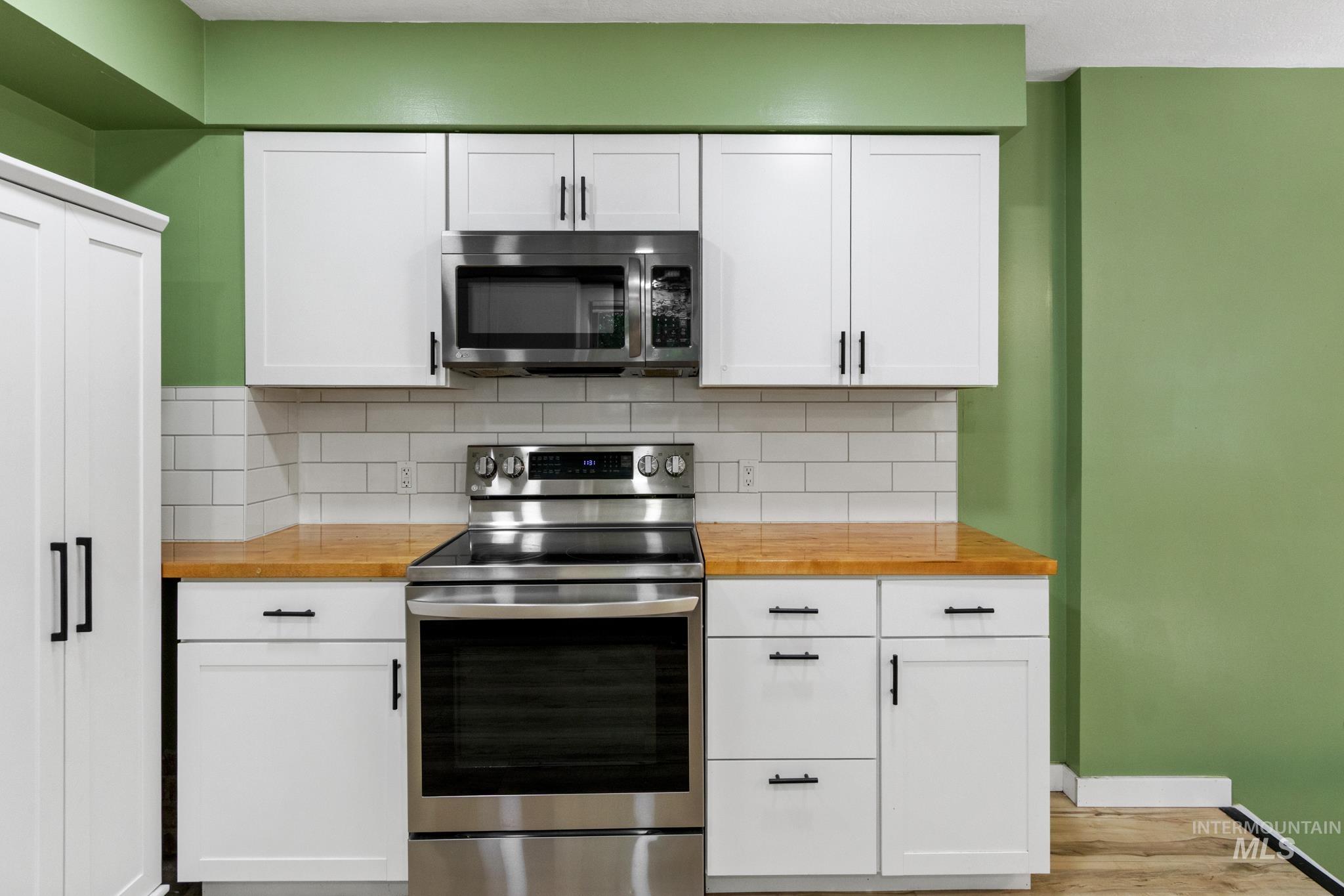 Kitchen featuring white shaker cabinetry, stainless steel appliances, butcher block countertops, and a subway tile backsplash