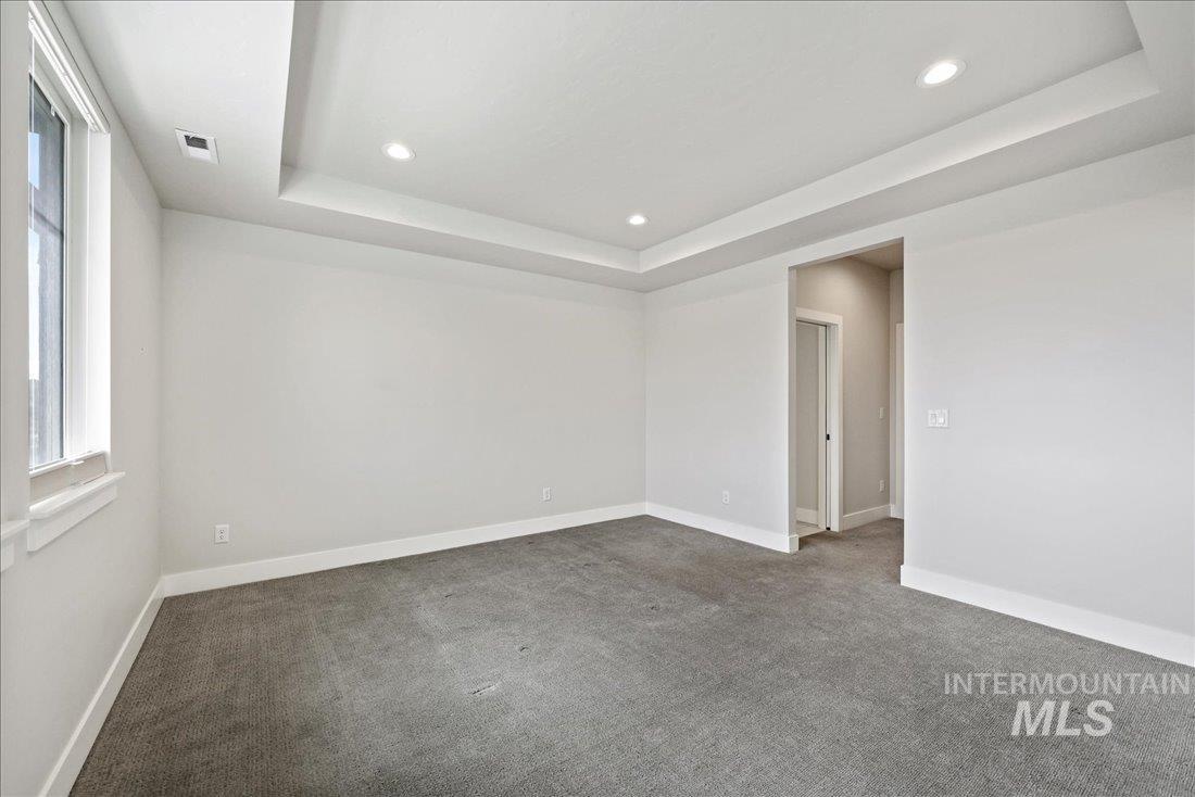 Empty room featuring a raised ceiling, dark colored carpet, and recessed lighting