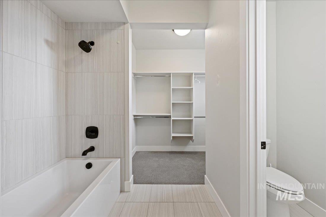 Bathroom with tub / shower combination, a spacious closet, light tile patterned floors, and light colored carpet