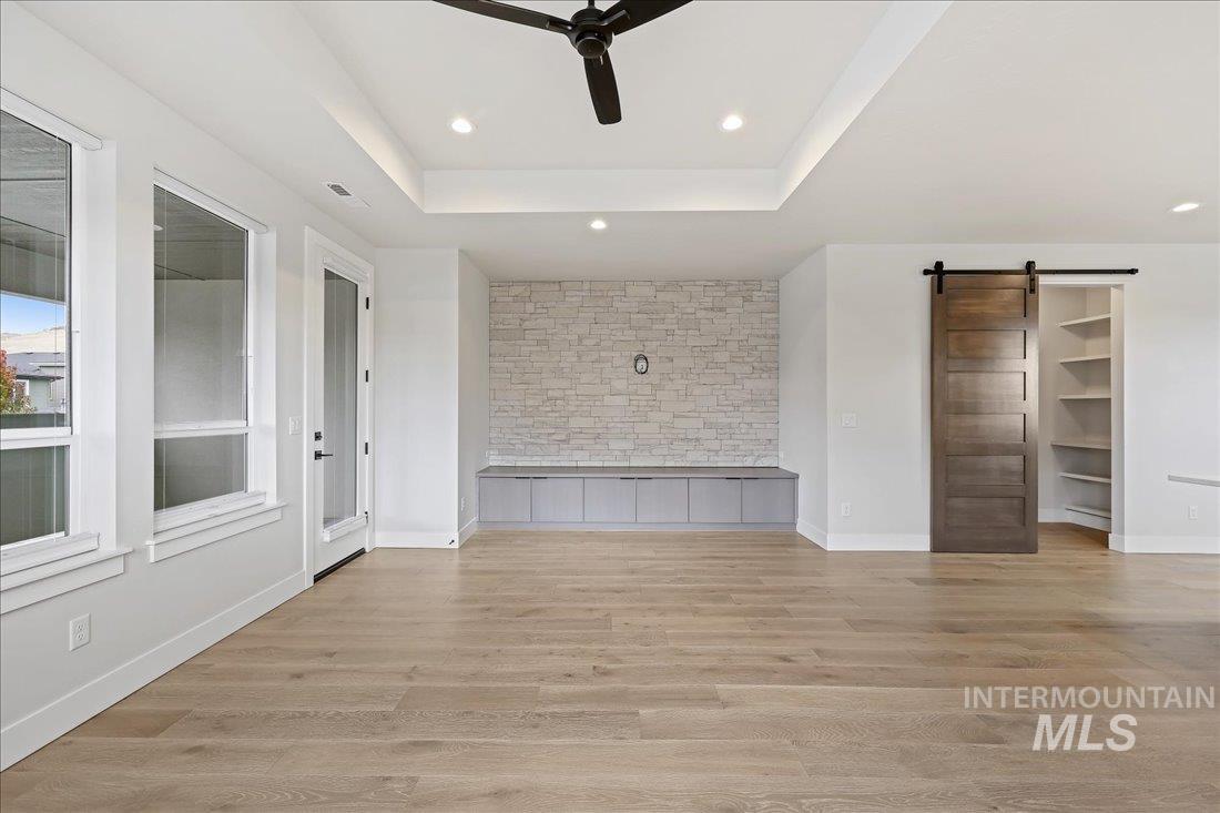 Unfurnished living room featuring a barn door, a tray ceiling, light wood-style flooring, and recessed lighting
