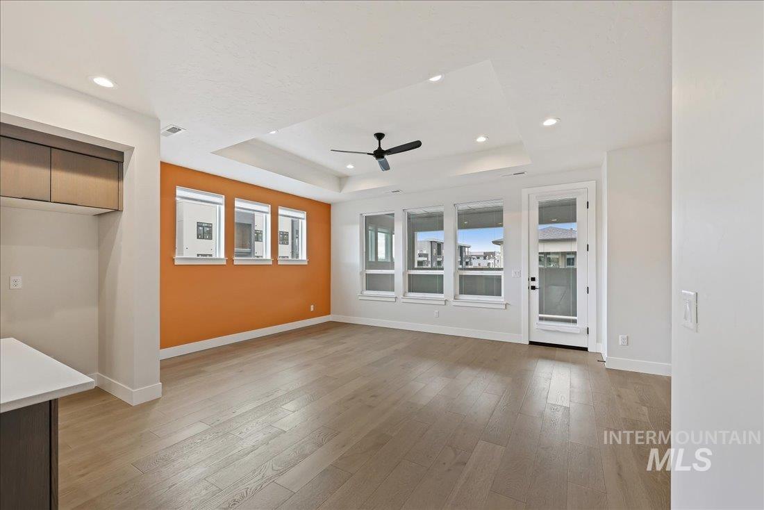 Unfurnished living room featuring a raised ceiling, light wood finished floors, a ceiling fan, and recessed lighting