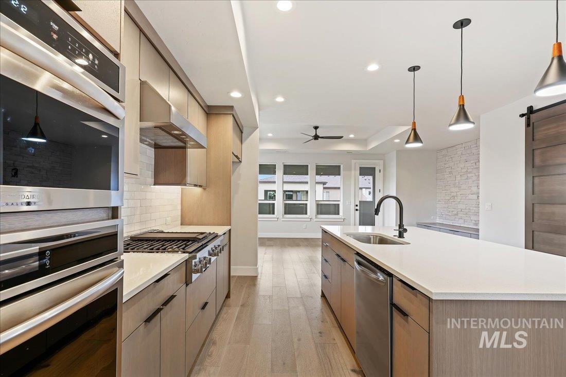 Kitchen with a barn door, pendant lighting, stainless steel appliances, light wood-type flooring, and modern cabinets