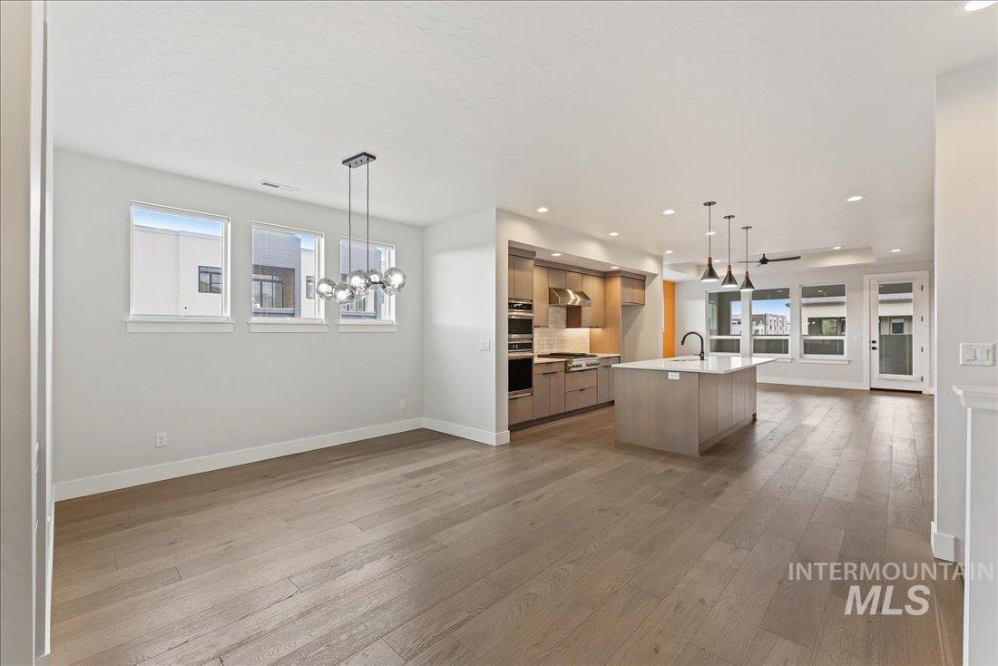 Kitchen featuring open floor plan, modern cabinets, decorative light fixtures, a kitchen island with sink, and light wood-style floors