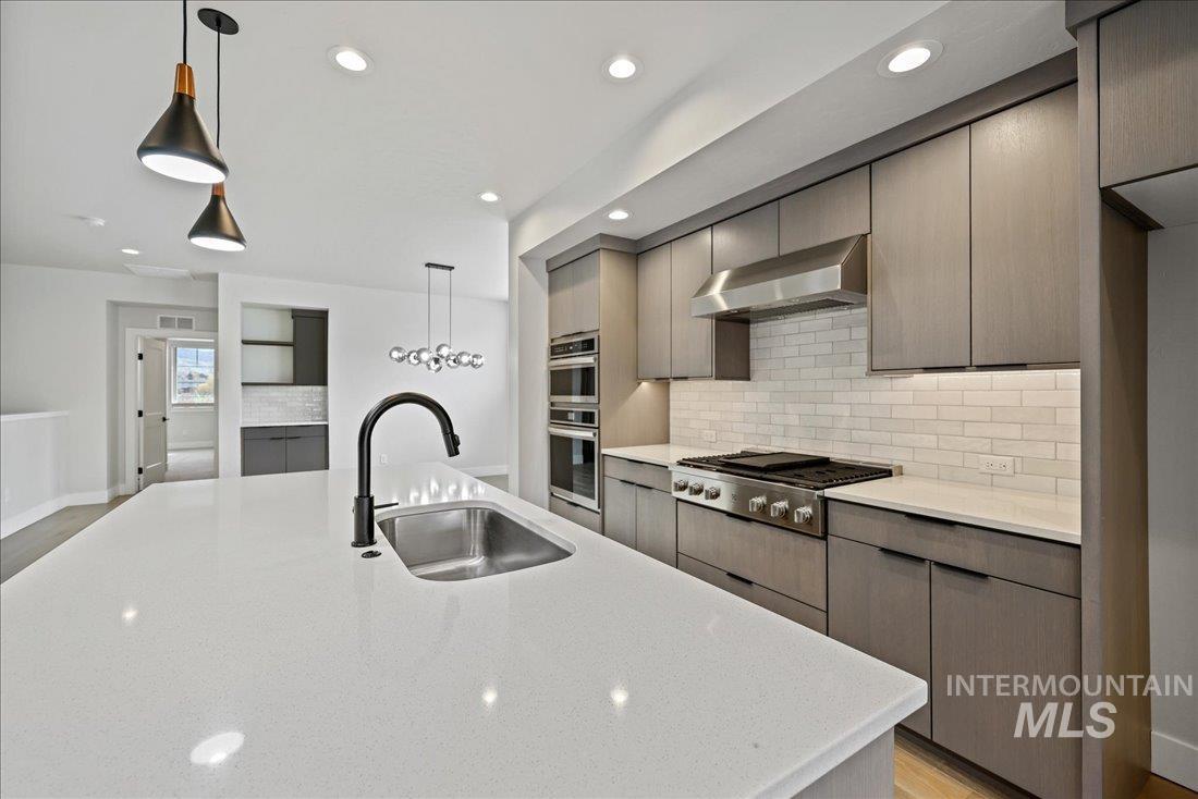 Kitchen featuring decorative light fixtures, backsplash, wall chimney range hood, light wood finished floors, and recessed lighting