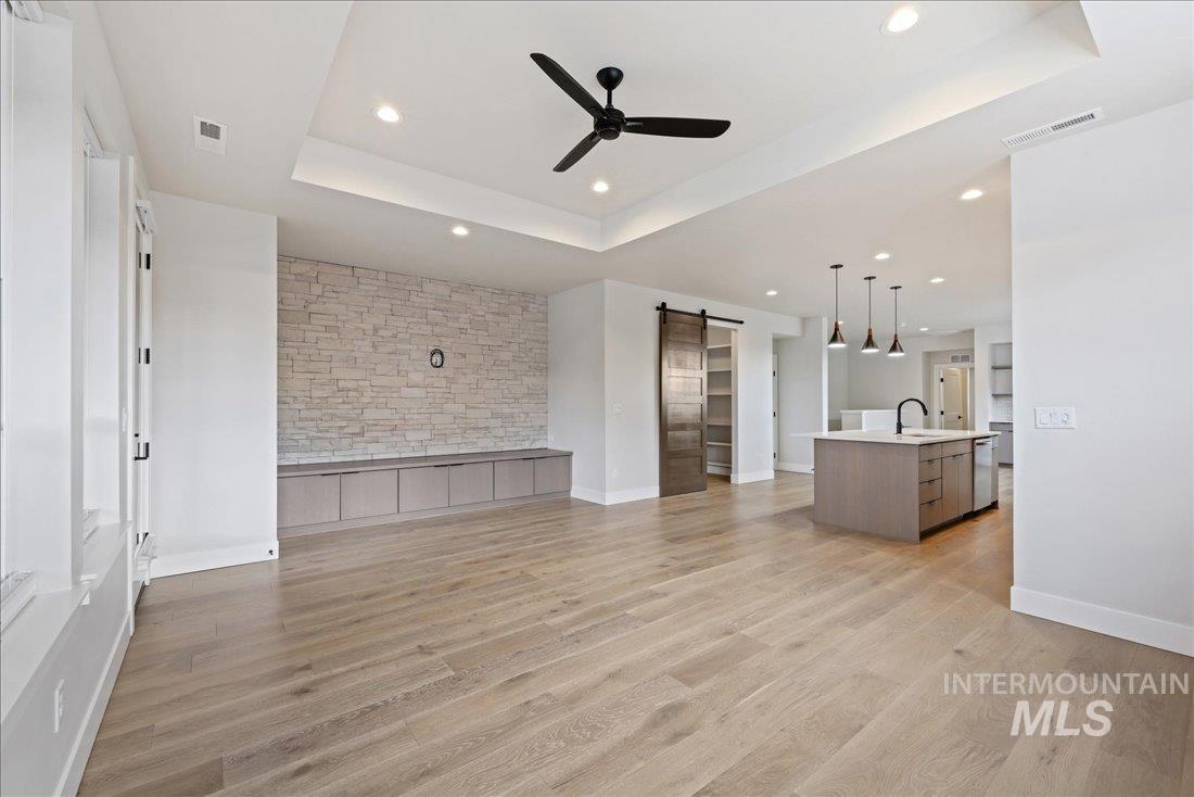 Unfurnished living room with a barn door, a raised ceiling, light wood finished floors, ceiling fan, and recessed lighting