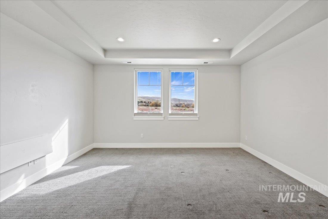 Empty room with light colored carpet, a raised ceiling, and recessed lighting