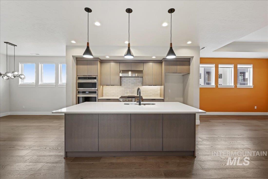 Kitchen with pendant lighting, modern cabinets, an island with sink, decorative backsplash, and recessed lighting