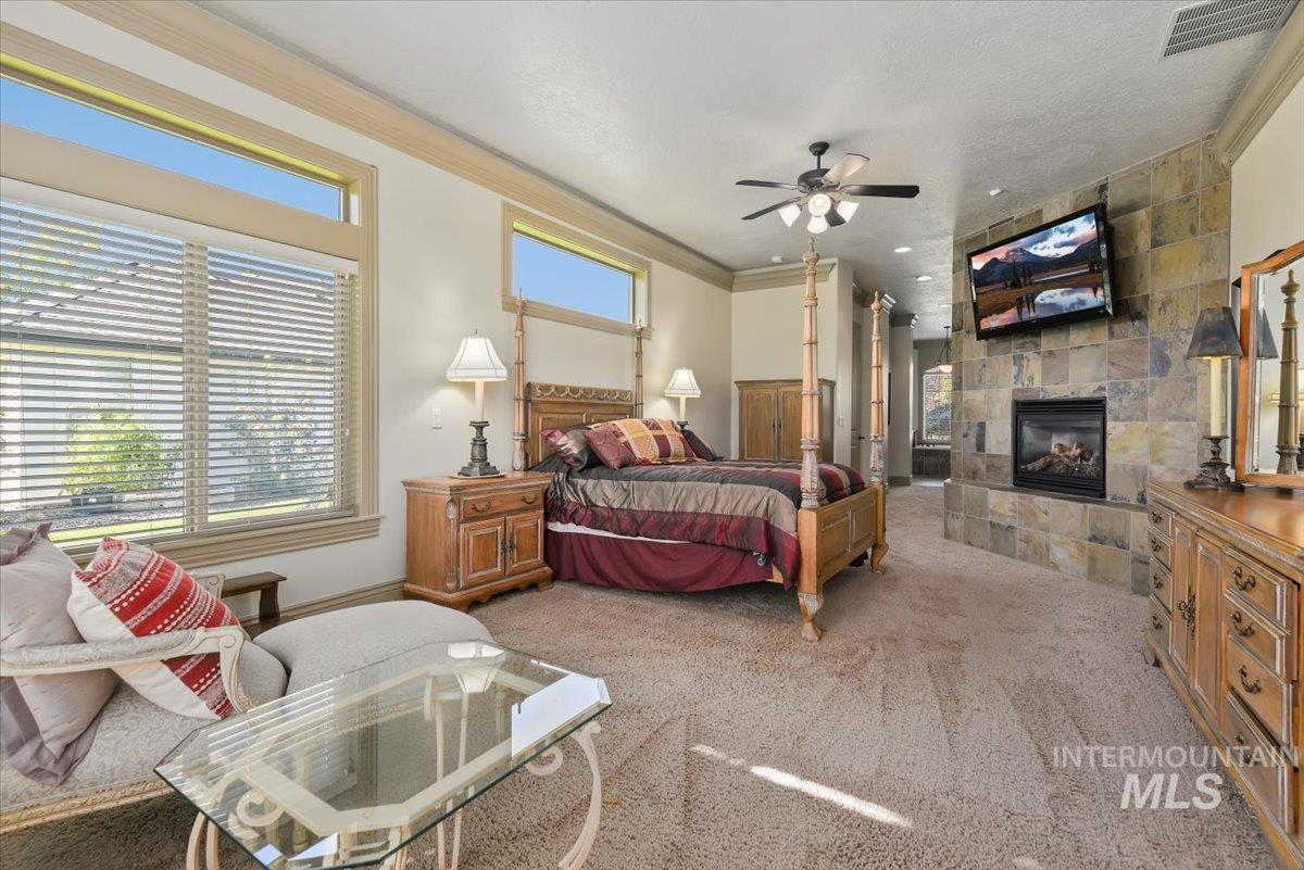 Bedroom with crown molding, light colored carpet, a tiled fireplace, and ceiling fan