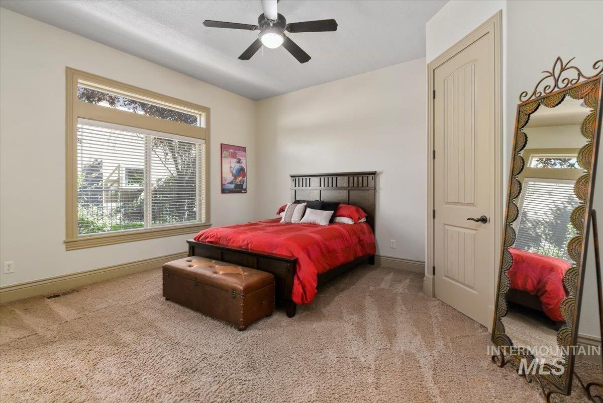 Bedroom with light carpet, multiple windows, ensuite bath and a ceiling fan