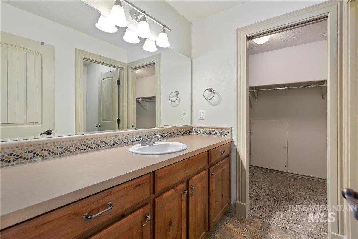 Full bathroom featuring a spacious closet, vanity, and dark stone finish floors