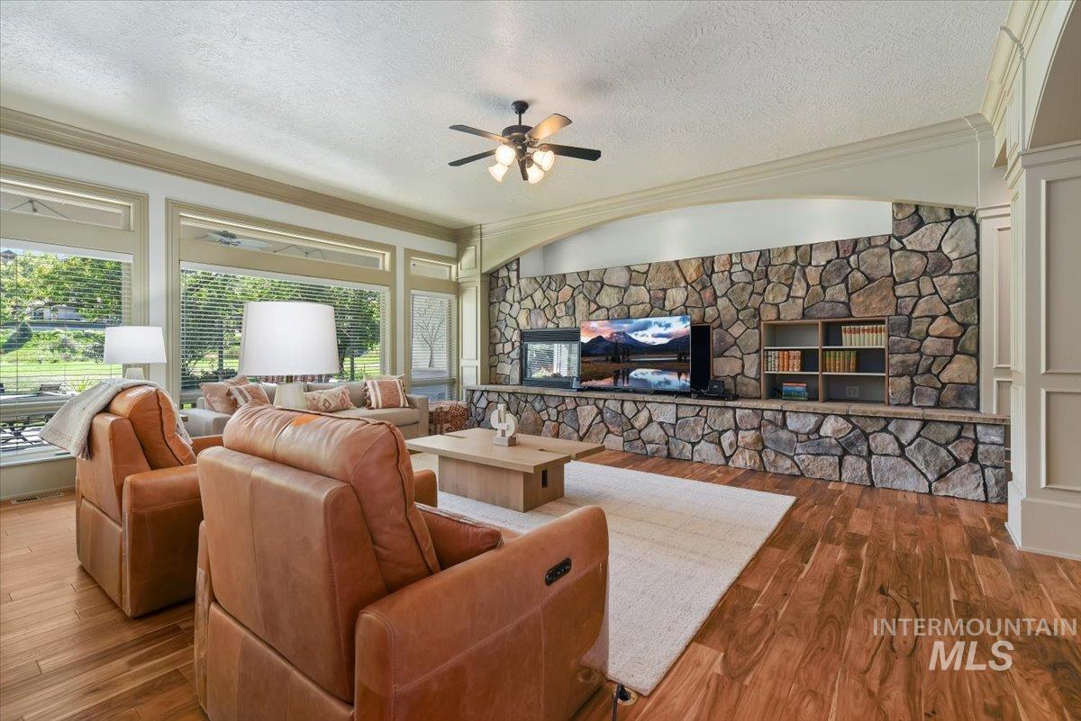 Living room with a textured ceiling, ornamental molding, ceiling fan, and dark wood-style flooring