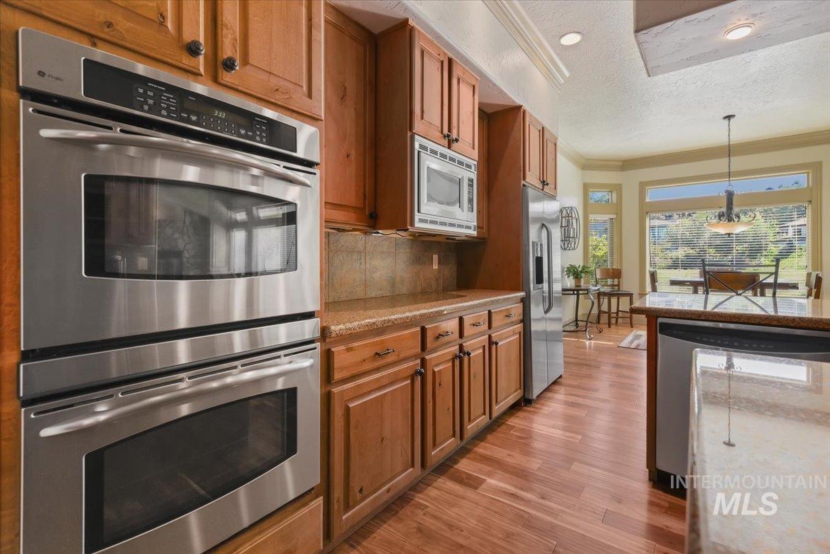 Kitchen with stainless steel appliances, crown molding, hanging light fixtures, decorative backsplash, and brown cabinetry