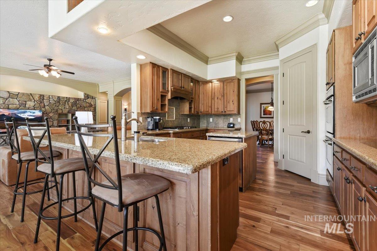 Kitchen with arched walkways, crown molding, brown cabinets, a peninsula, and a kitchen bar