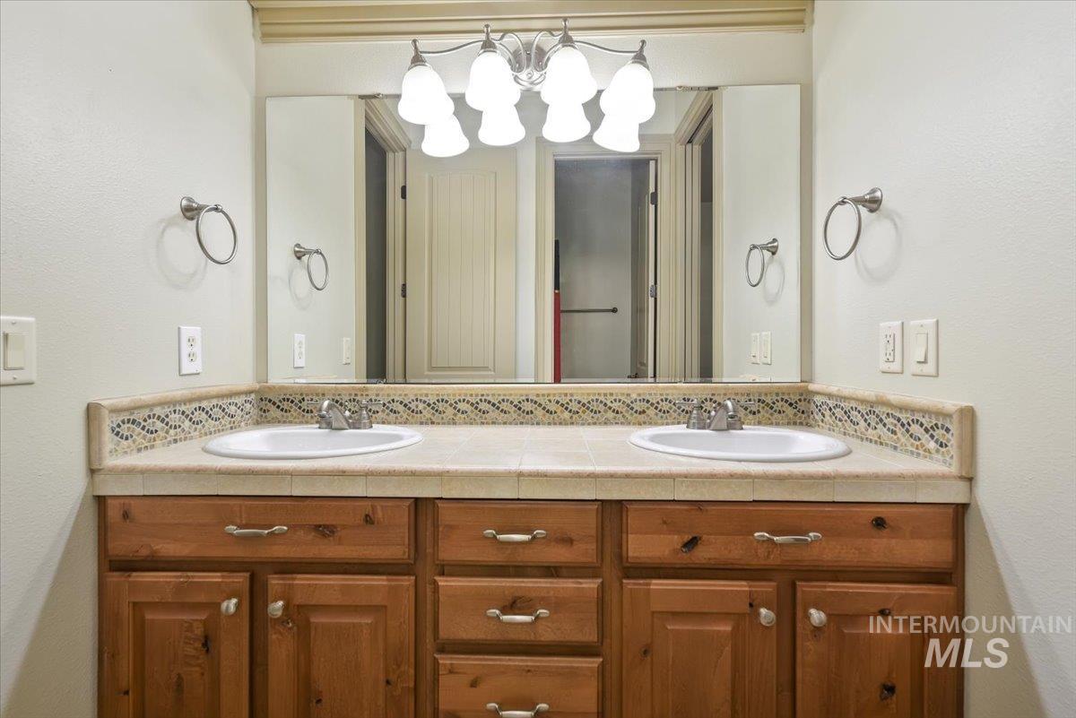 Bathroom featuring double vanity, a textured wall, tasteful backsplash, and a chandelier