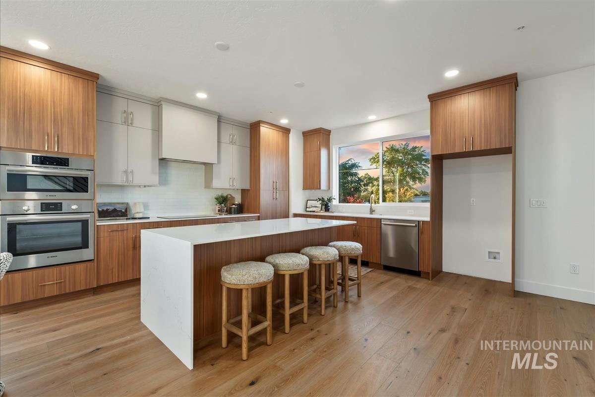 Kitchen with brown cabinetry, a breakfast bar area, a center island, light wood-type flooring, and appliances with stainless steel finishes