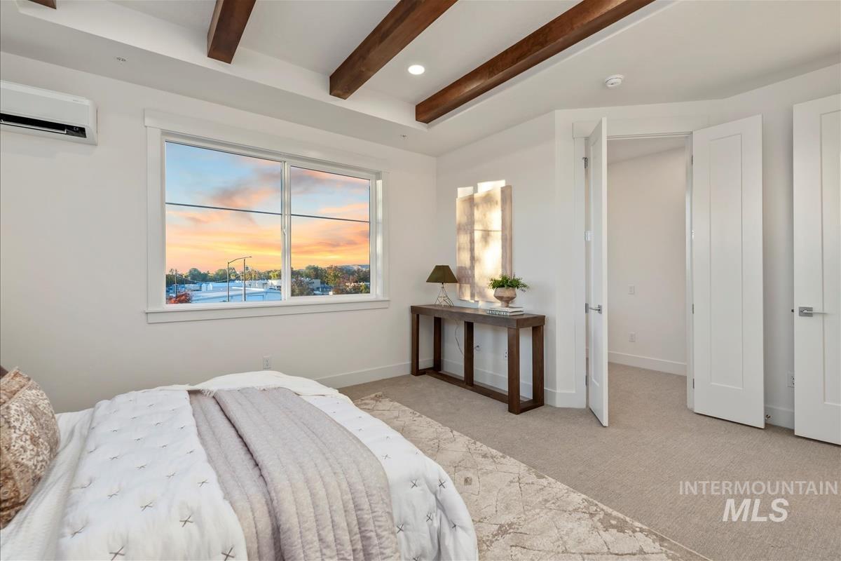 Bedroom featuring light colored carpet, beamed ceiling, a wall mounted AC, and recessed lighting