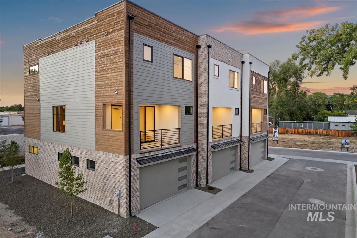 Contemporary house featuring a balcony, an attached garage, brick siding, and driveway