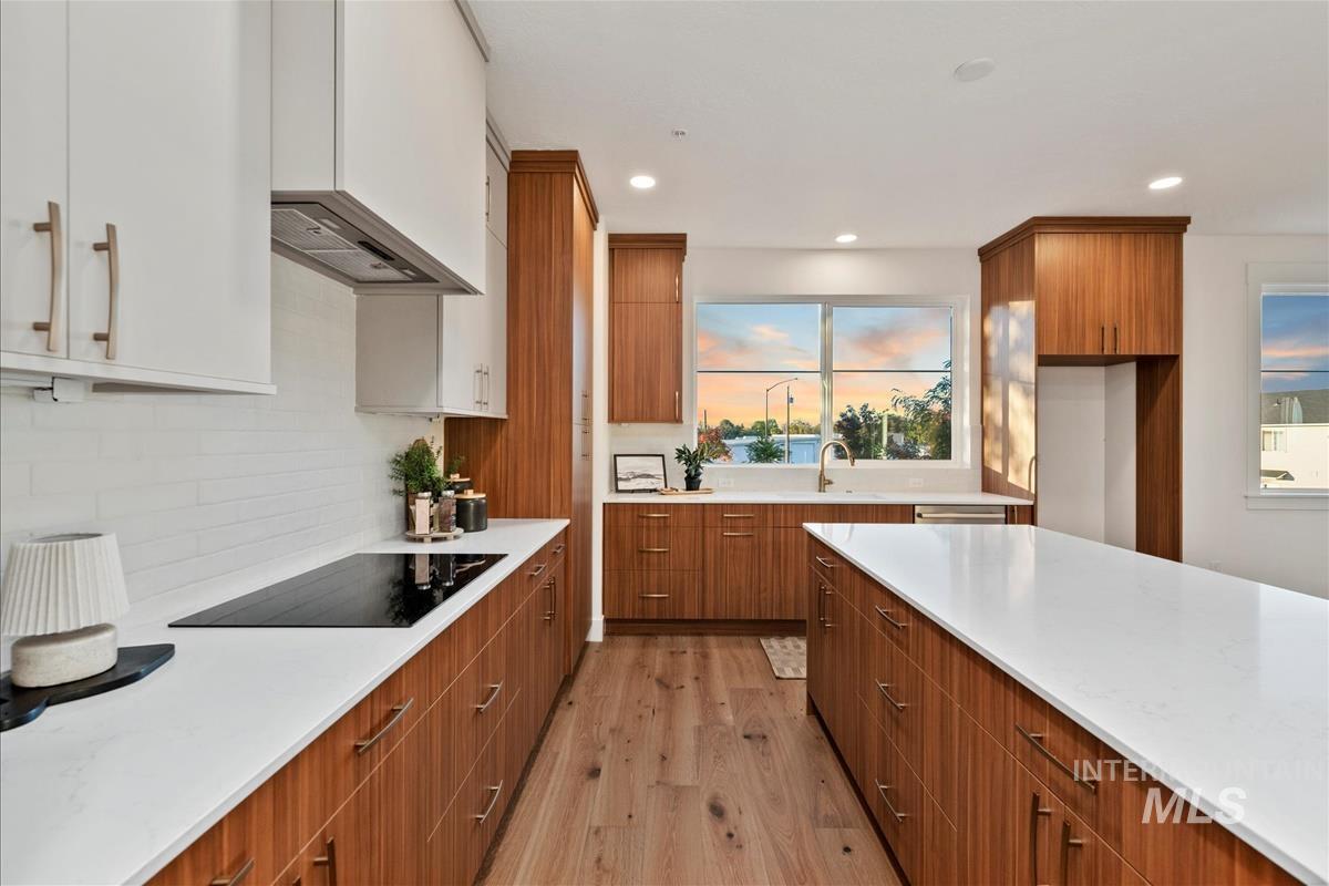 Kitchen with brown cabinets, light wood-style floors, light stone counters, recessed lighting, and black electric stovetop
