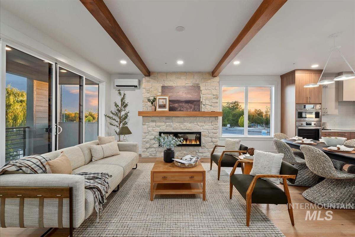 Living area with beamed ceiling, light wood-style flooring, a stone fireplace, a wall mounted air conditioner, and recessed lighting