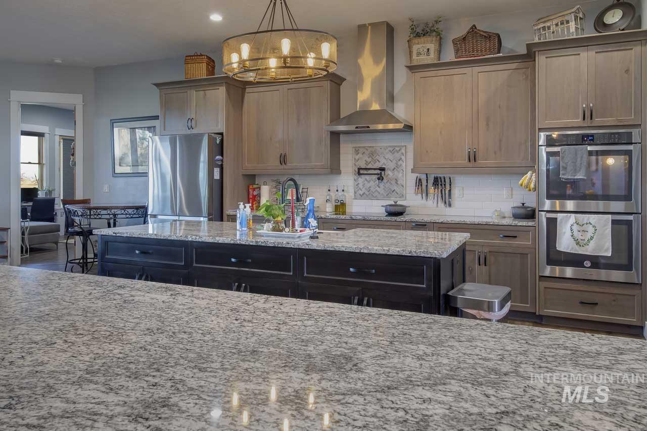Kitchen featuring wall chimney range hood, appliances with stainless steel finishes, tasteful backsplash, light stone countertops, and recessed lighting
