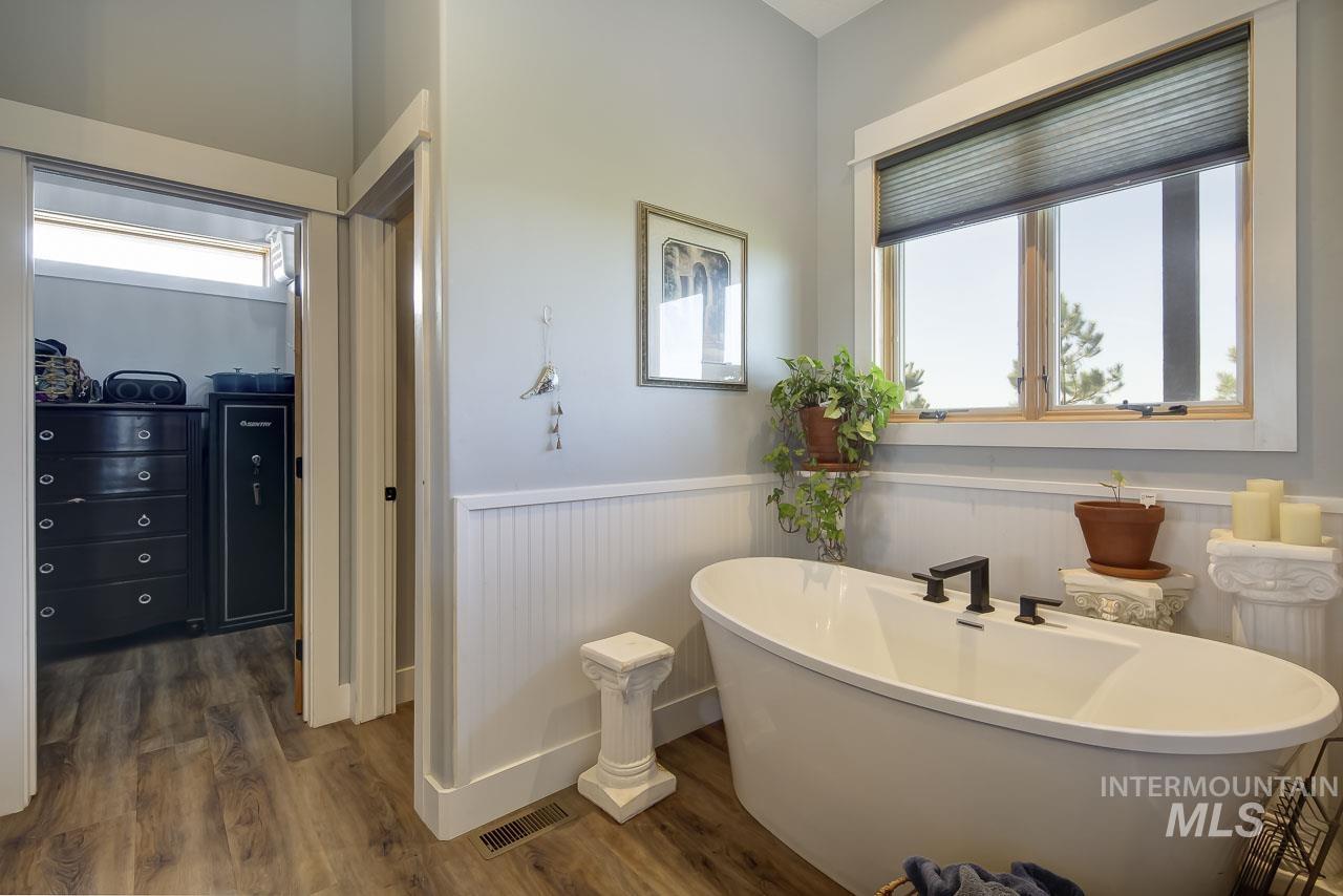 Bathroom with wainscoting, a freestanding tub, and dark wood-style flooring