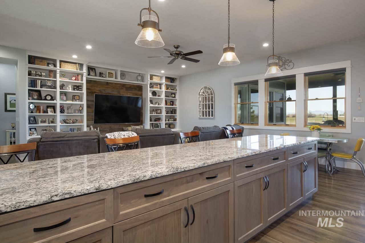 Kitchen featuring light stone countertops, built in features, decorative light fixtures, open floor plan, and dark wood-style floors