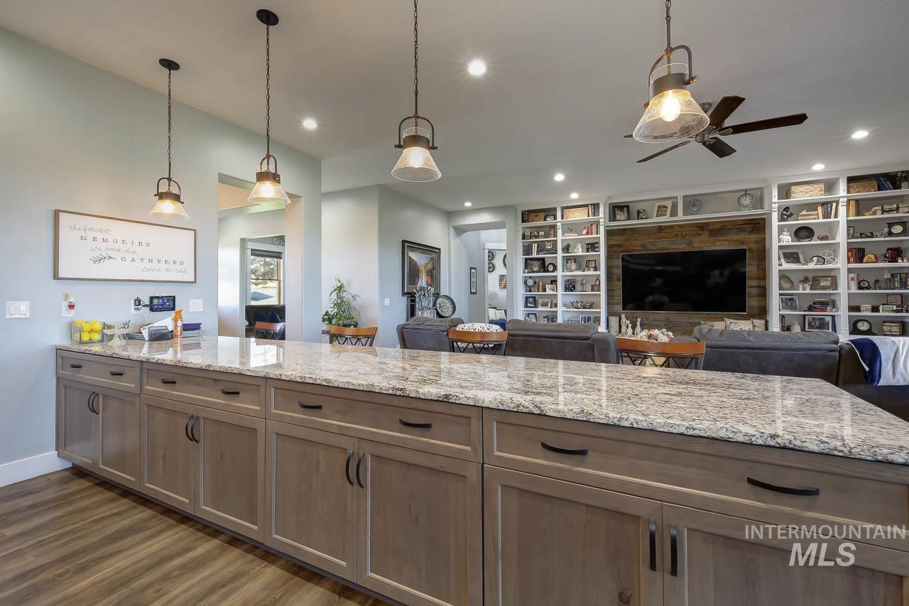 Kitchen with hanging light fixtures, light stone counters, dark wood-type flooring, open floor plan, and recessed lighting