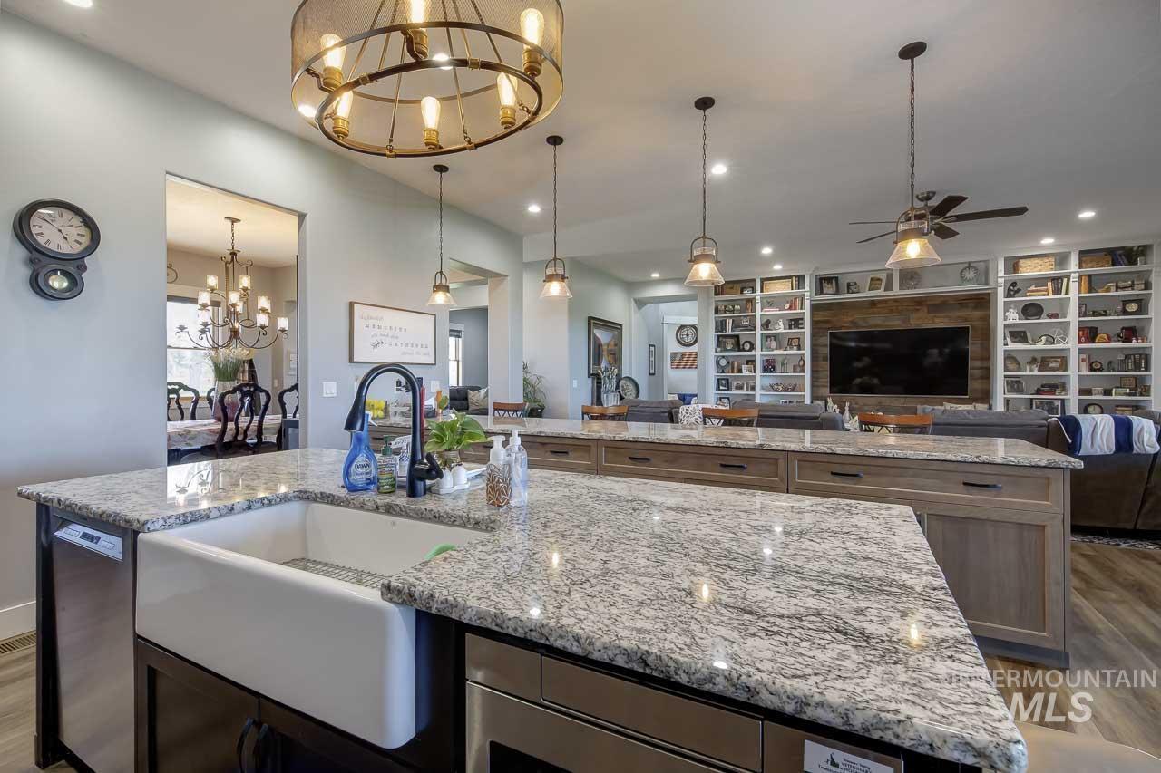 Kitchen featuring dark wood-style flooring, open floor plan, an island with sink, a chandelier, and light stone countertops