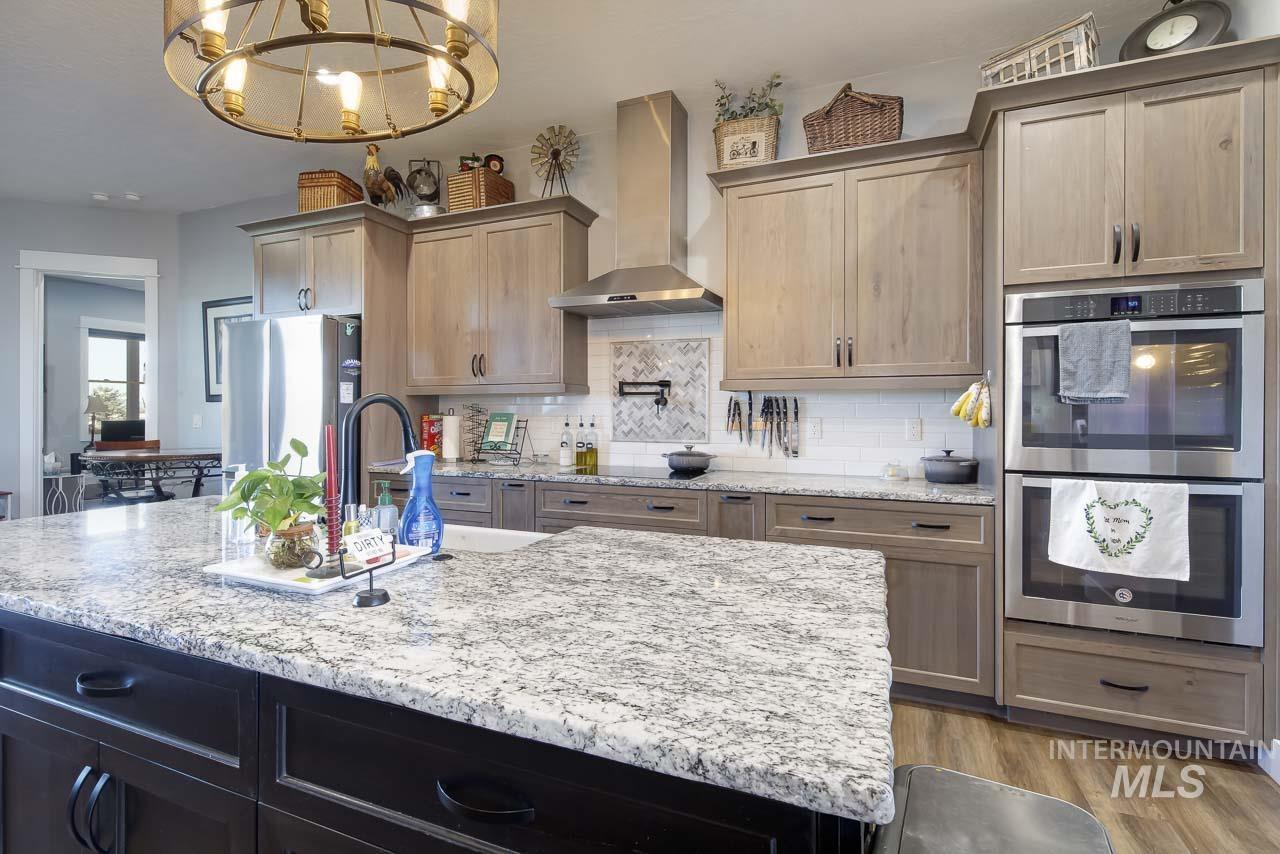 Kitchen with appliances with stainless steel finishes, wall chimney range hood, light stone countertops, and decorative backsplash
