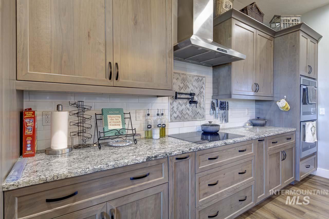 Kitchen featuring wall chimney range hood, backsplash, light stone countertops, double oven, and light wood finished floors