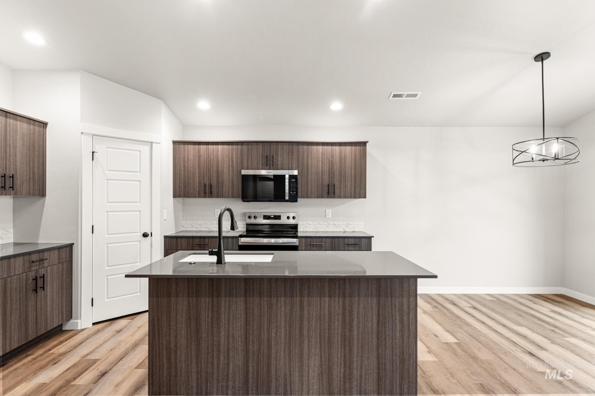Kitchen with decorative light fixtures, stainless steel appliances, a center island with sink, dark stone counters, and recessed lighting