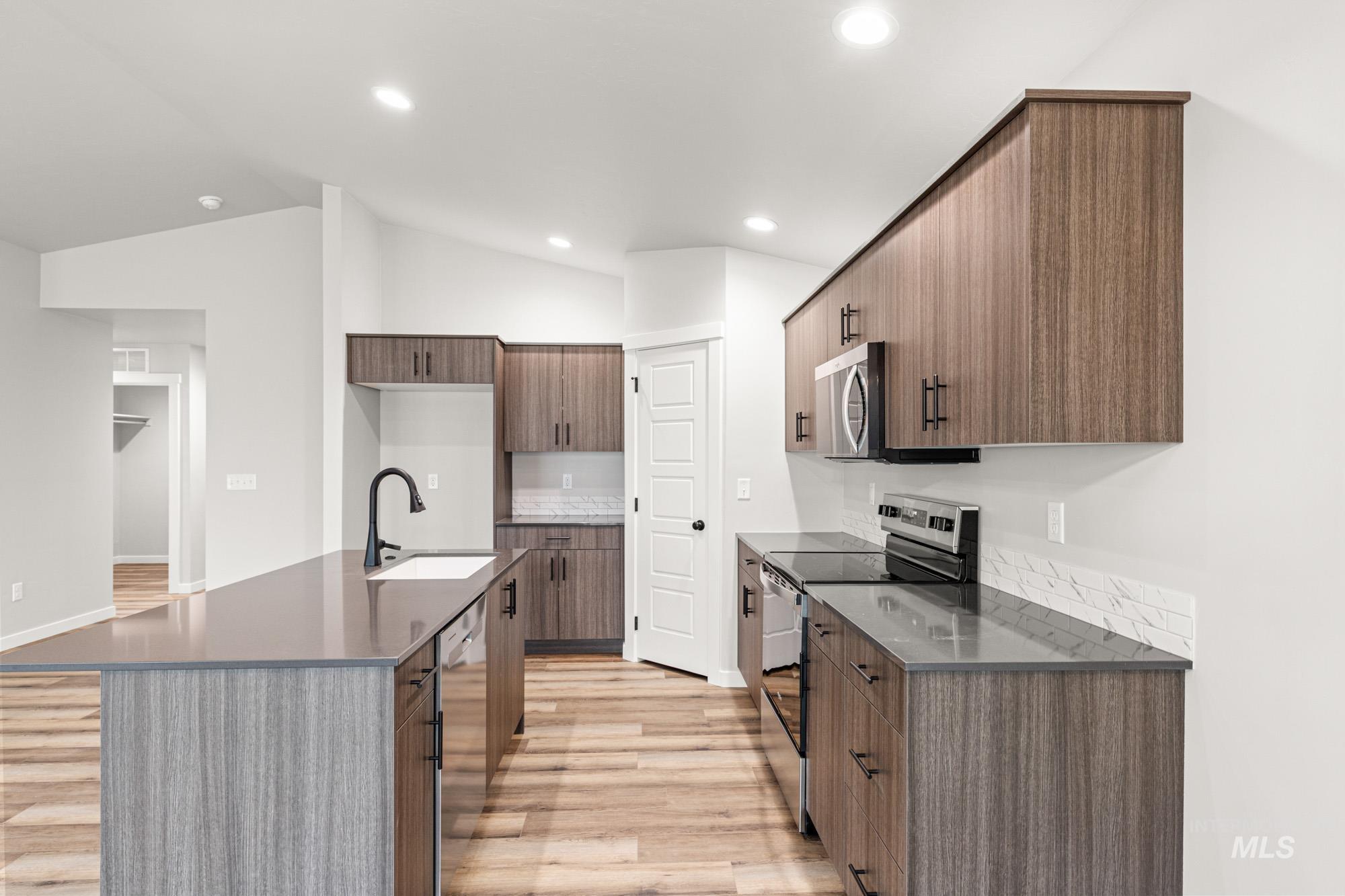 Kitchen featuring appliances with stainless steel finishes, light wood-style flooring, dark stone counters, modern cabinets, and a center island with sink