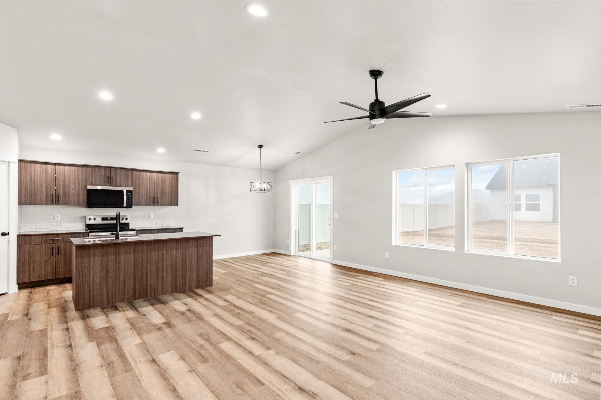 Kitchen with open floor plan, a kitchen island with sink, appliances with stainless steel finishes, light wood-style flooring, and vaulted ceiling