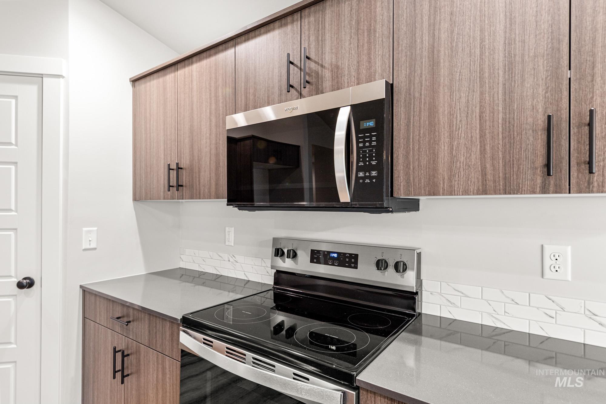 Kitchen with stainless steel appliances, modern cabinets, dark stone countertops, and brown cabinets