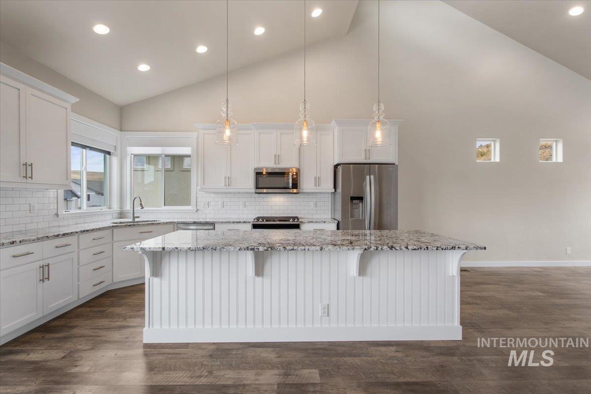 Kitchen with appliances with stainless steel finishes, a center island, white cabinetry, a breakfast bar area, and pendant lighting