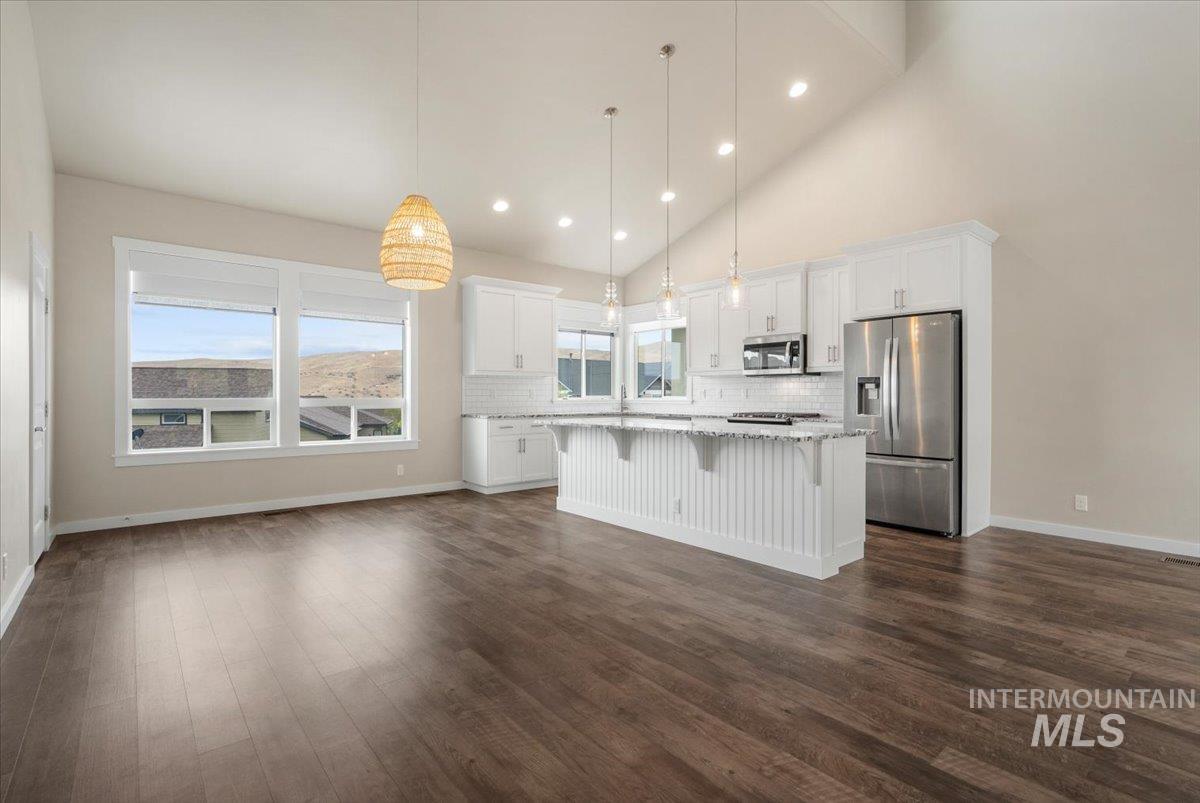 Kitchen featuring tasteful backsplash, hanging light fixtures, a breakfast bar area, stainless steel appliances, and white cabinets