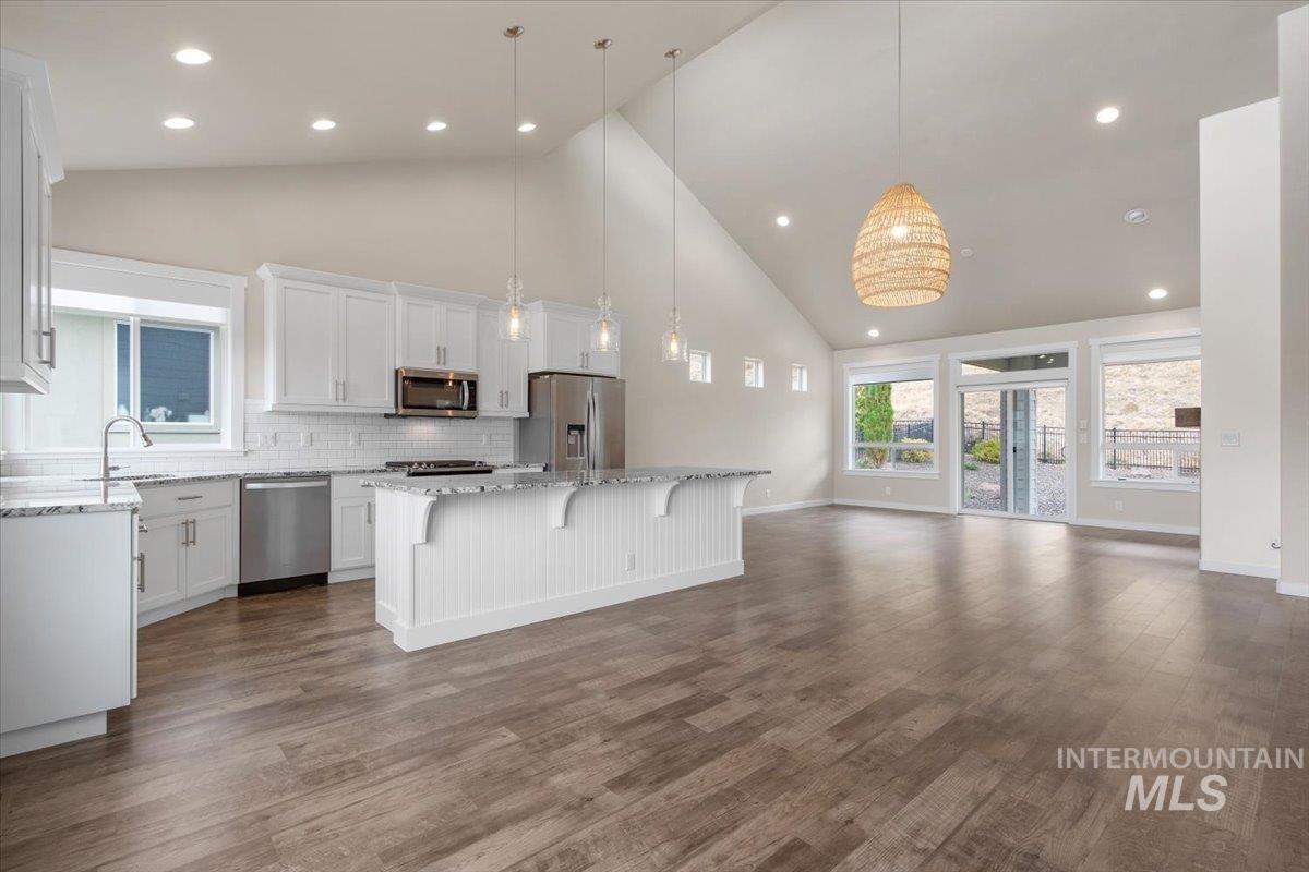 Kitchen featuring high vaulted ceiling, white cabinetry, hanging light fixtures, backsplash, and appliances with stainless steel finishes