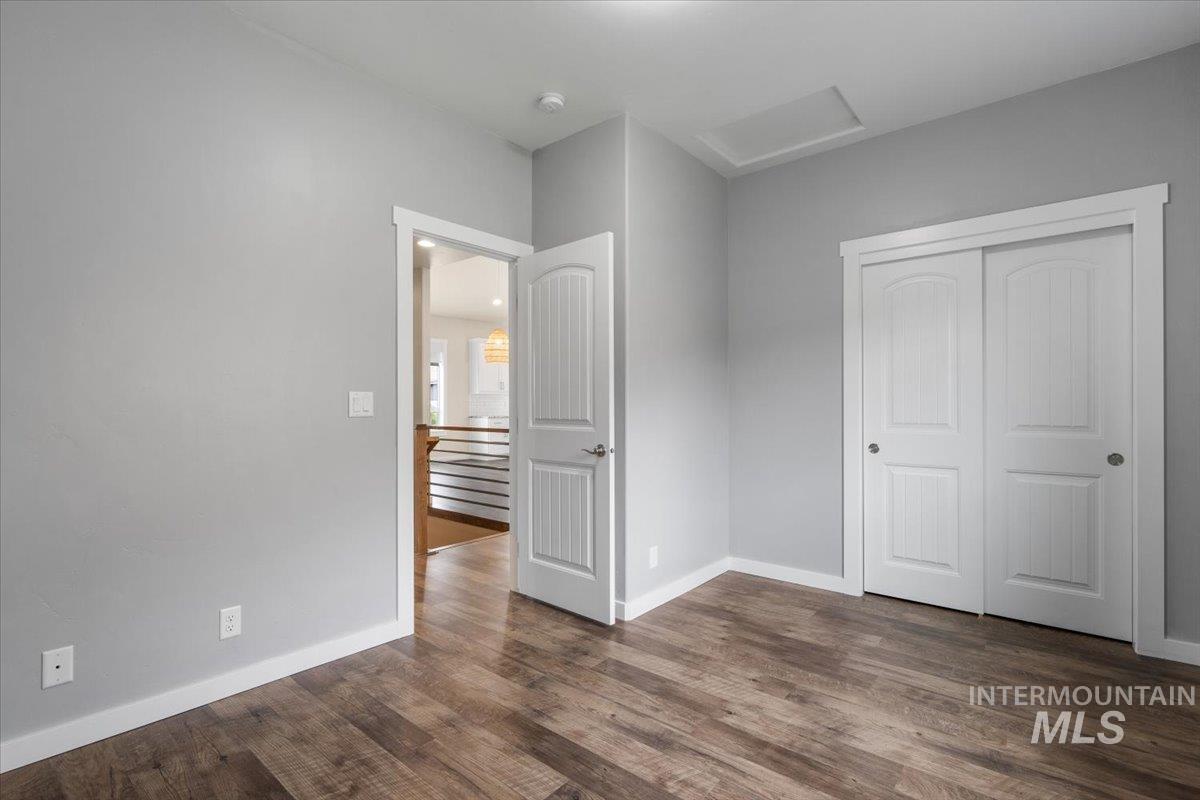 Unfurnished bedroom featuring attic access, a closet, and dark wood finished floors
