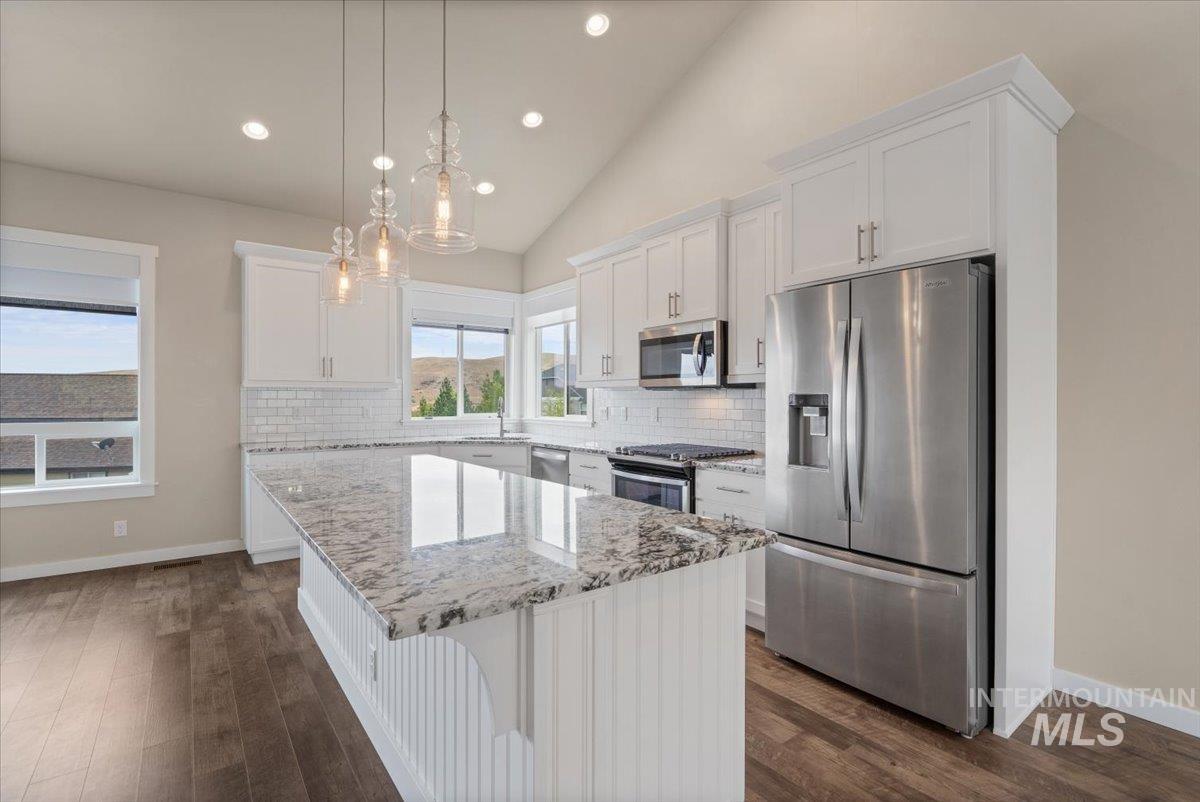 Kitchen featuring stainless steel appliances, light stone countertops, white cabinets, a center island, and backsplash