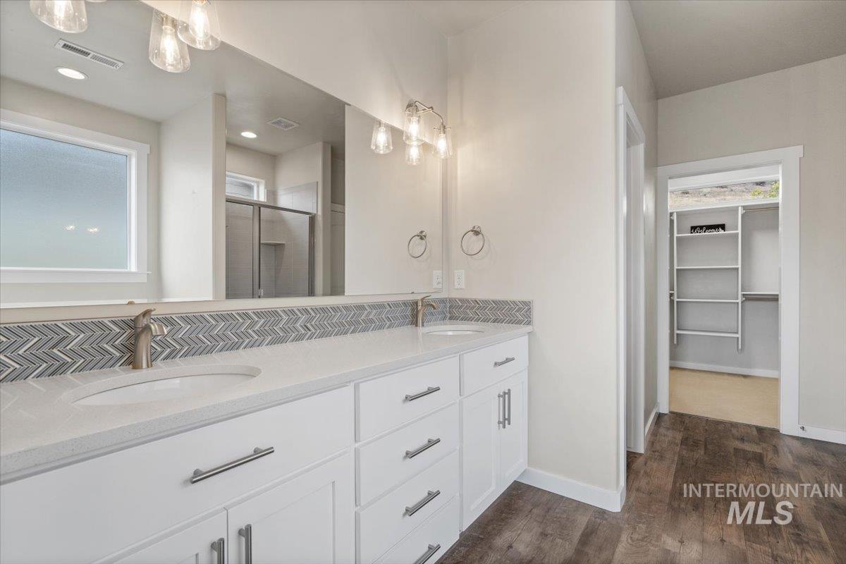 Full bathroom featuring a walk in closet, a stall shower, double vanity, dark wood finished floors, and recessed lighting