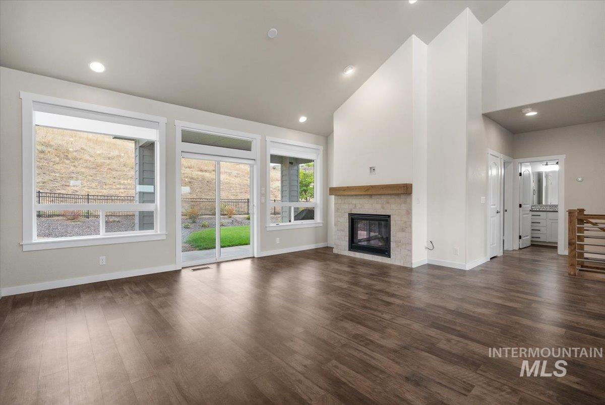 Unfurnished living room with recessed lighting, high vaulted ceiling, dark wood finished floors, and a glass covered fireplace