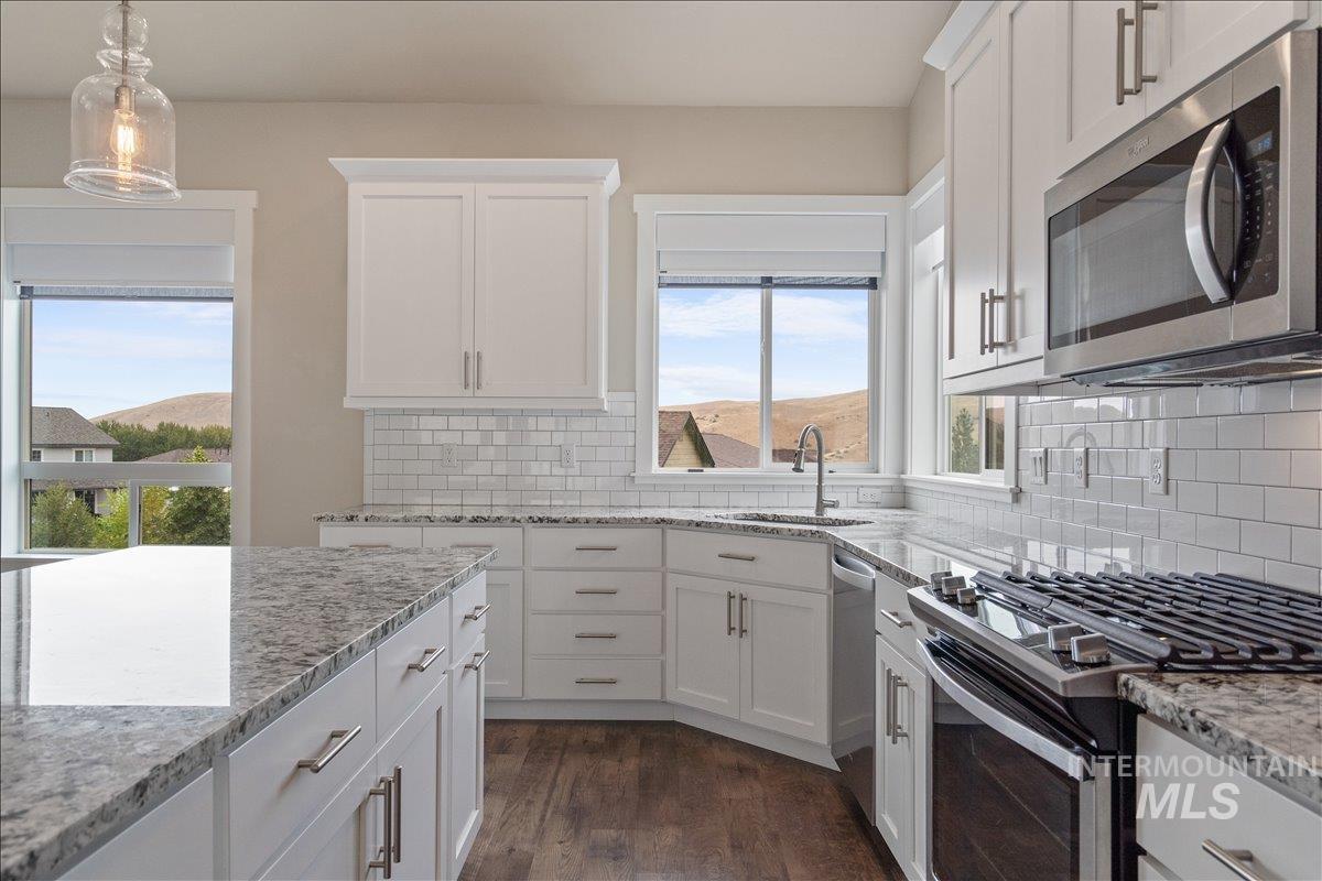 Kitchen with appliances with stainless steel finishes, light stone counters, white cabinets, dark wood-style floors, and a mountain view
