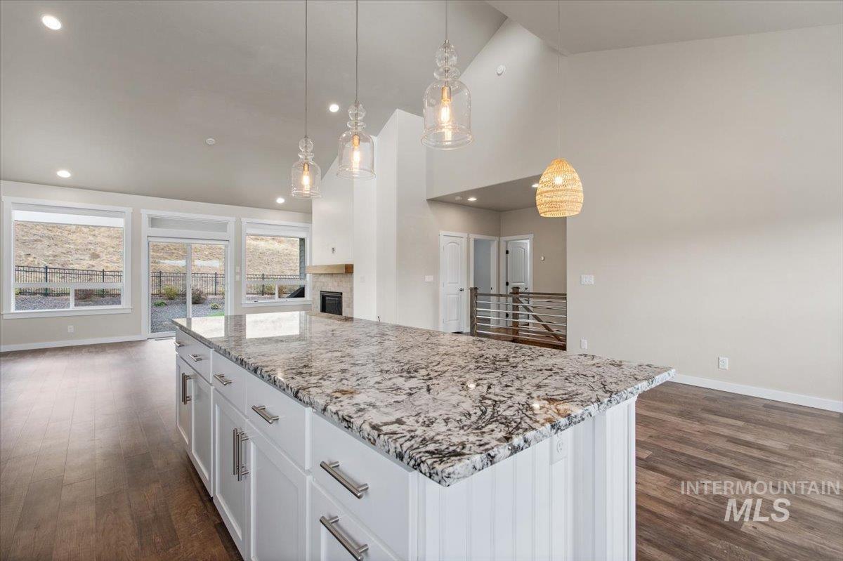 Kitchen featuring a center island, a fireplace, decorative light fixtures, light stone countertops, and high vaulted ceiling