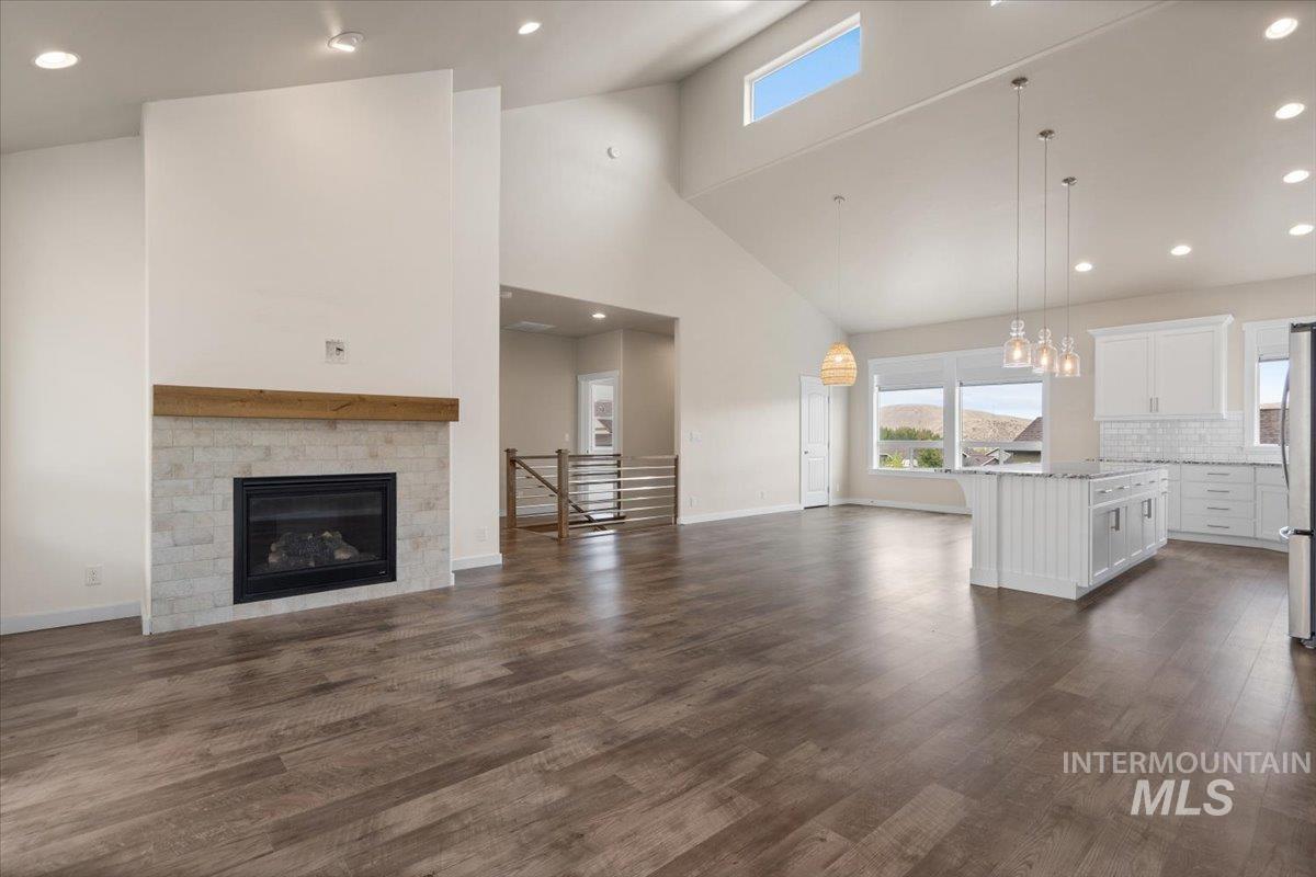 Unfurnished living room with recessed lighting, high vaulted ceiling, plenty of natural light, dark wood-style flooring, and a glass covered fireplace