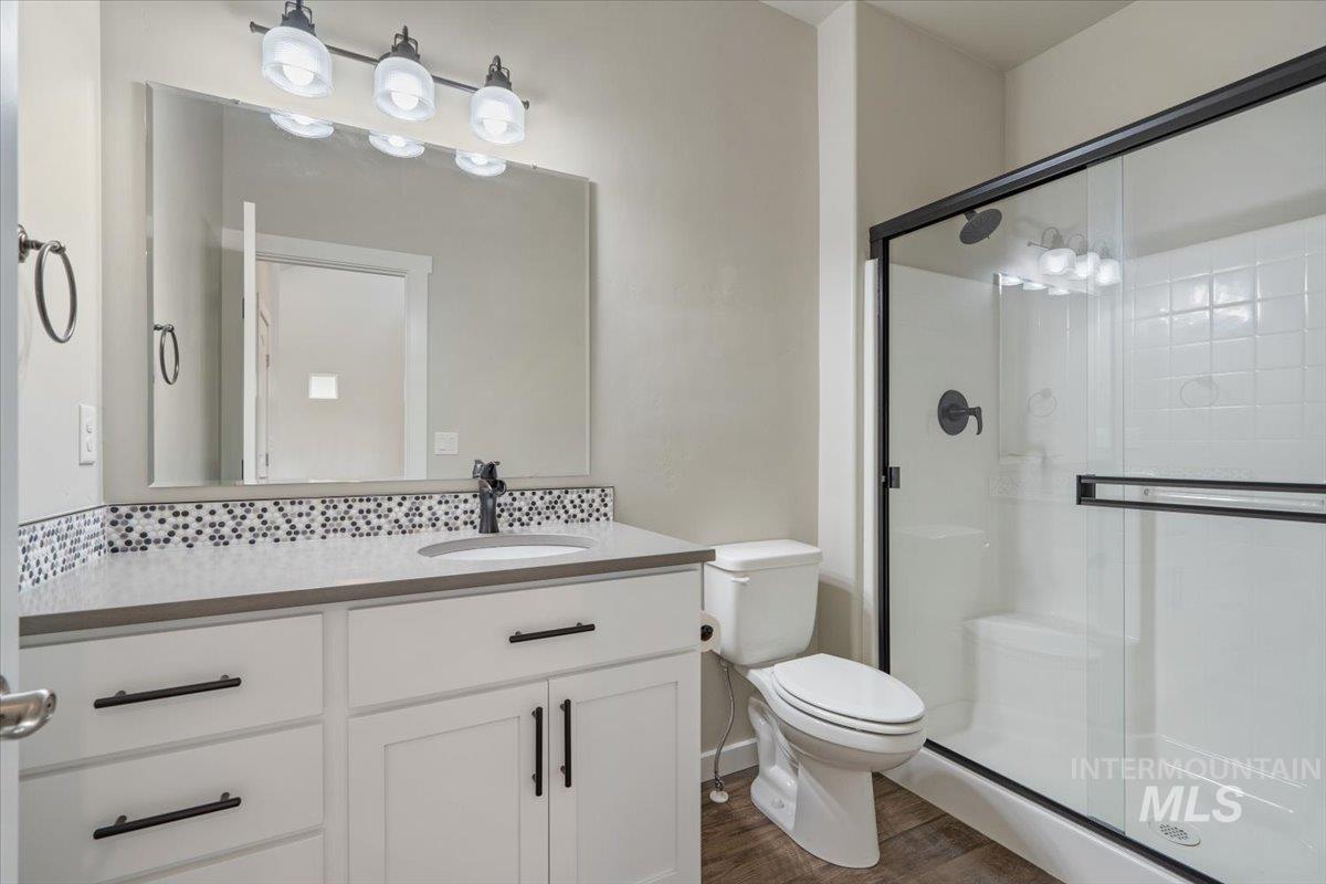 Full bathroom featuring a stall shower, vanity, dark wood-type flooring, and backsplash