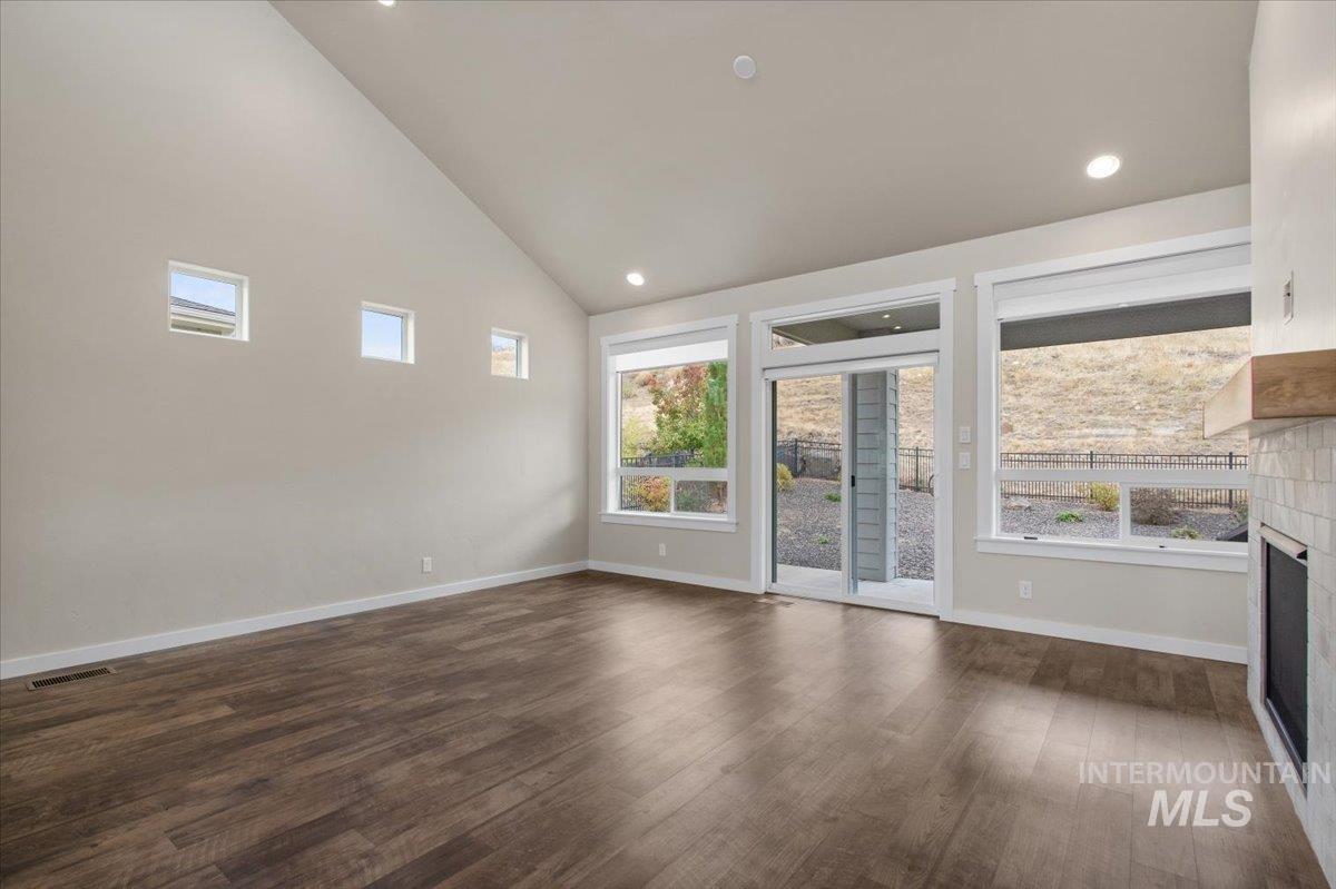 Unfurnished living room with a tiled fireplace, high vaulted ceiling, recessed lighting, and dark wood-style floors